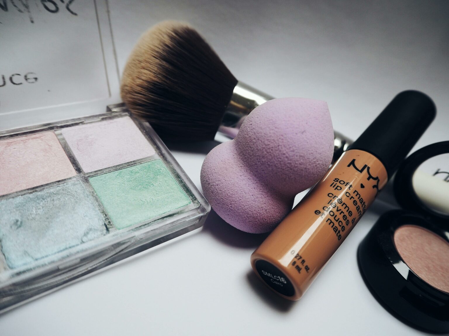Palette di ombretti, spugnetta, fondotinta e pennelli per il trucco appoggiati su un piano